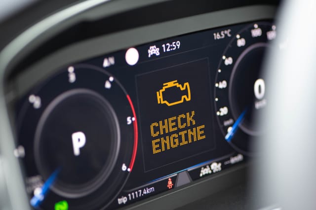 Close-up of a luxury car's digital dashboard cluster displaying an illuminated amber check engine light warning icon and text.