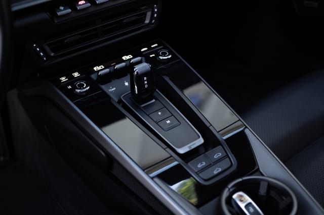 Close-up of a modern Porsche high-performance vehicle center console featuring a sleek electronic gear shifter with drive controls and illuminated digital readouts.
