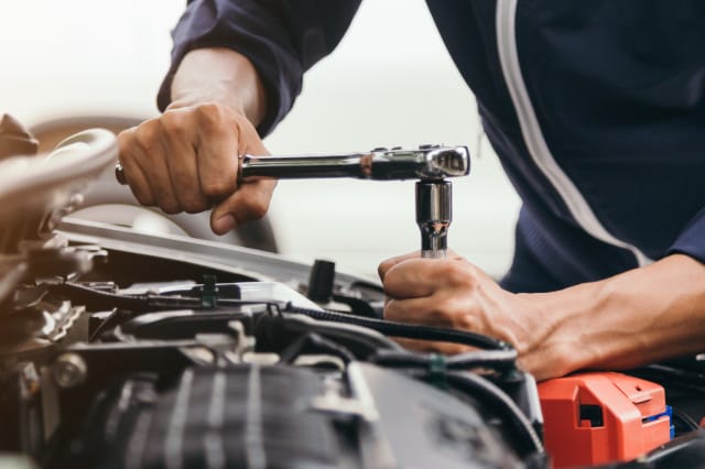 Close-up of an auto mechanic using a ratchet socket wrench to service components inside a car's open engine bay.