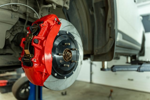 Close-up of a high-performance brake assembly featuring a bright red multi-piston caliper and slotted rotor on a vehicle elevated on a lift for inspection.